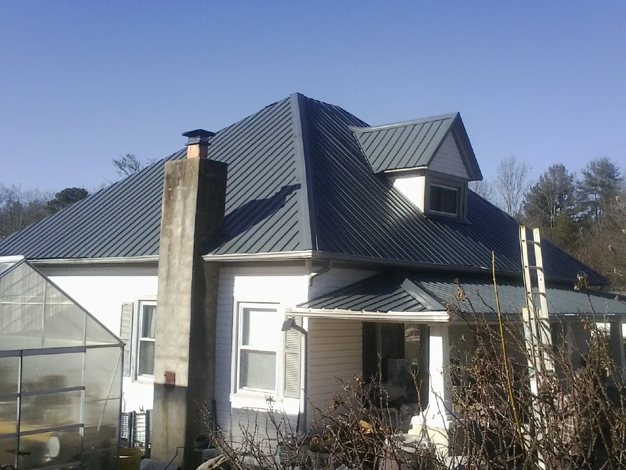 Dark blue standing seam metal roof on a white farmhouse with dormer — Slate & Tile Roof Repair by Roofing Brothers in Jordan